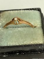 Front view of gold ring in box showing seed pearl and setting
