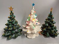 Three ceramic Christmas trees side-by-side showing colours, sizes, presence/absence of bases