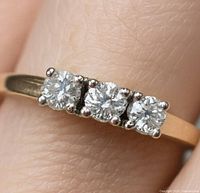 Close-up of ring on finger showing three round diamonds and yellow gold band