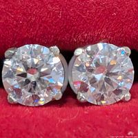 Close-up of two round brilliant moissanite stones in four-prong 14K gold stud settings against a red background
