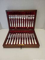 Open wood case displaying 12 forks in lid and 12 knives in base