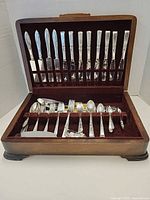 Open wooden flatware chest showing knives in lid slots and mixed flatware in lower tray
