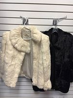 White rabbit fur jacket and black fur jacket hanging on slat wall