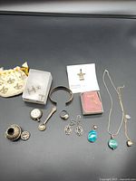 All items laid out: silver salt shaker, spoon, watch, cufflinks, tie tack, bracelet, cross pendant, two necklaces, earrings, pouch