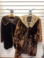 Two knee-length fur coats hanging, showing colors and collars