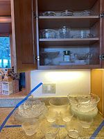 Cabinet and countertop view showing assortment of glass bowls, compote, sugar shaker
