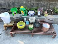 Overview of bench with assorted planters, vases, watering can, fertilizer jug