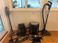 Group shot of stick vacuum, canister vacuum, shredder, hoses and accessories