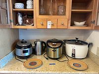 Countertop view showing three rice cookers, electric kettle and two ceramic plates
