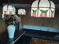 Kitchen view showing three hanging stained glass pendant lights and white vase with faux flowers
