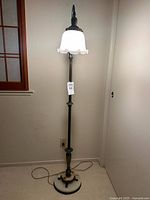 Full view of brass bridge floor lamp standing upright, light on