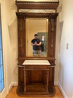 Full frontal view of wooden hall tree showing mirror, marble console, hooks and umbrella rails