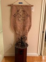 Full view of macramé wall hanging above side table with silver tea set