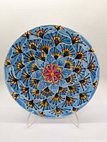 Front view of handpainted ceramic wall plate showing blue peacock feather design