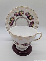 Teacup in front of saucer showing fruit garland and gold filigree