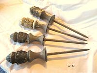 five decorative metal hose stakes laid side by side showing full length and finials