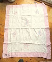 Full view of white quilt with pink border laid flat
