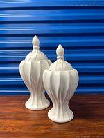 Front view of both white ceramic pedestal jars with lids showing size difference and fluted design
