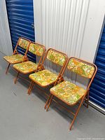 Four orange floral Samsonite folding chairs lined up