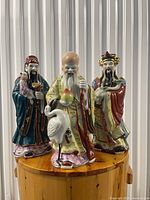 Group shot of three porcelain Fu, Lu, Shou figurines on wooden surface