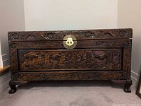 Front view of carved storage chest with brass latch and carved feet