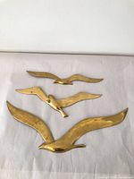 Three brass bird wall art pieces laid out on white background