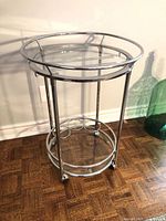 Full view of chrome and glass round bar cart showing both shelves and casters