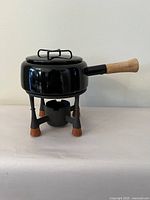 Side view of black enamel fondue pot on stand with burner