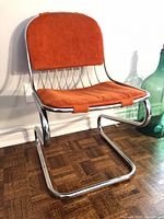 Full view of chrome cantilever chair showing orange cushions and frame design