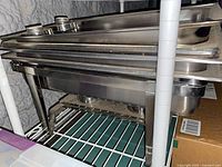 Stack of stainless chafing pans and frame on shelf