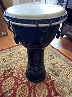 Full view of black djembe showing shell carvings, tuning hardware and white head