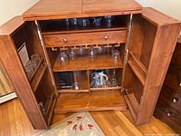Cabinet open showing interior drawer, glass rack, shelves