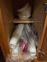 Cabinet with white paper cups, clear plastic cups, red plastic cups, stack of large coffee filters