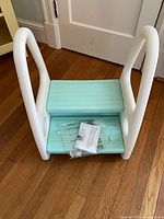 Stool lying on side showing two aqua steps and instruction sheet with hardware