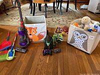 Full lot showing toy vacuum, cleaning tools, storage bins, RC dinosaurs, remotes and wood box of small toys