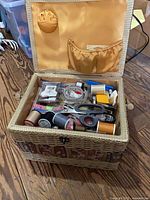 Open sewing basket showing contents: thread spools, scissors, tape measure, yellow lining with pin cushion