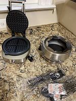 Breville waffle maker open alongside Cuisinart fondue pot on stand with packaged accessories