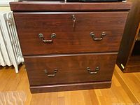 Front view of dark wood two-drawer lateral file cabinet with key visible in lock