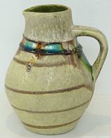 Full view of glazed beige ceramic jug with handle and drip-glazed shoulder