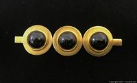 Front view of gold-tone brooch showing three black cabochon stones