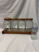 Front view of four lidded glass jars on wooden rack with water bottle for scale