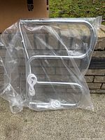 Front view of chrome S-shaped electric towel warmer in plastic wrap with power cord visible