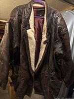Full view of brown leather jacket hanging, showing shearling lining and pockets