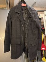 Front view of charcoal grey wool blend coat hanging, showing button and zip front, flap pockets