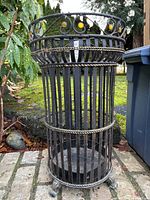 Full view of black metal umbrella stand showing slat construction and decorative accents