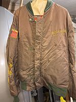 Front of brown bomber jacket showing buttons, green knit trim and embroidery