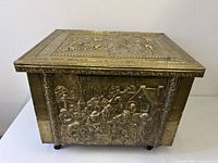 Front view showing embossed brass village scene and casters