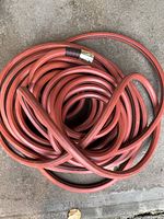 Coiled red rubber garden hose showing entire length and metal coupling