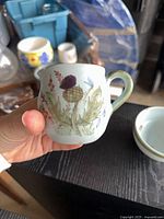 Hand shows small porcelain creamer with floral painting