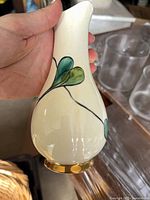 Front view of cream ceramic bud vase with green leaf motif and gold base